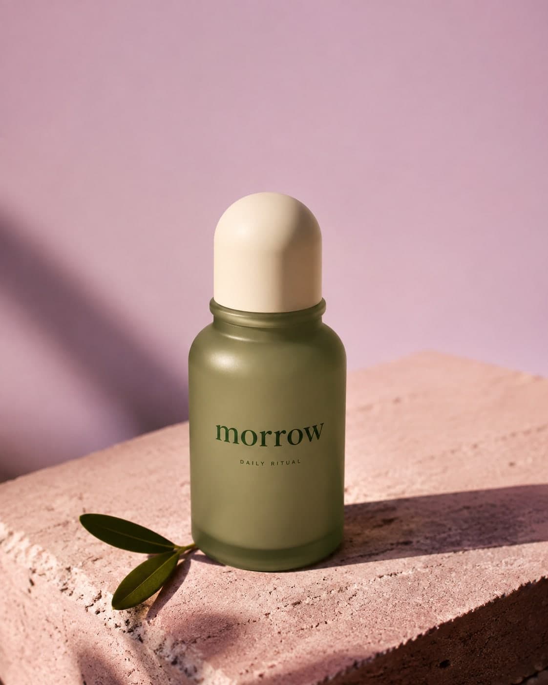 Morrow ad, a fictional brand: a green bottle on a pink stone with a sprig of leaves